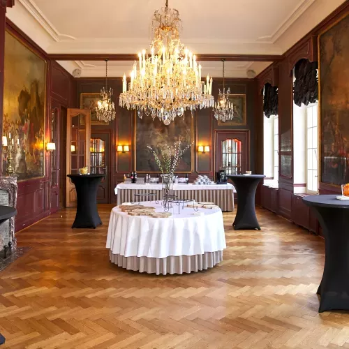 Salle de réception élégante avec parquet, lustres, tables rondes noires et boiseries