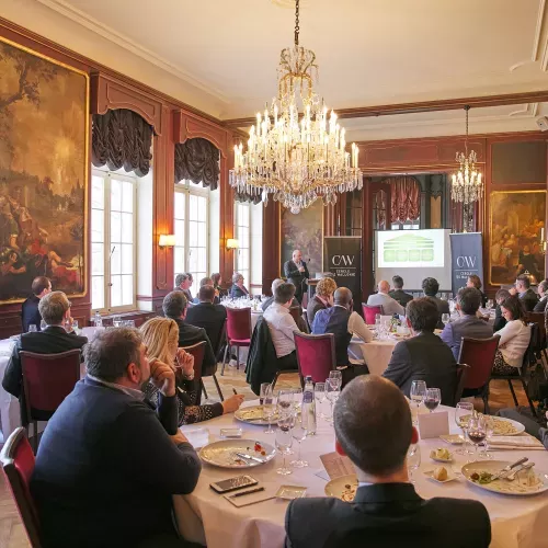 Réunion formelle dans une salle élégante avec lustre, tables dressées et nombreux participants assis