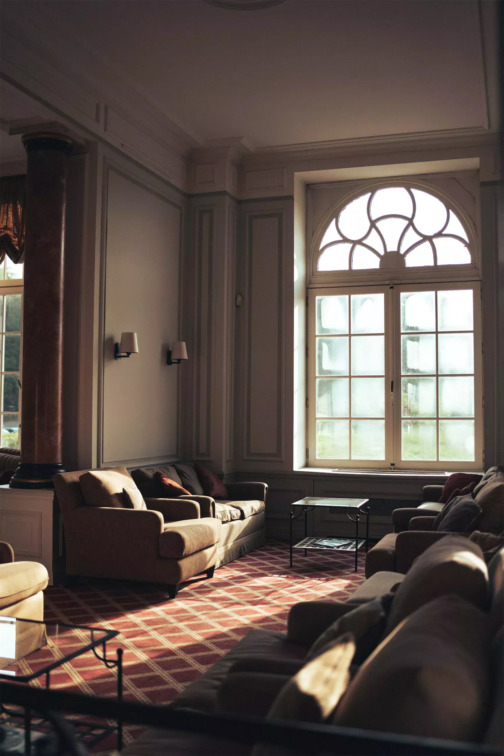 Salon lumineux avec canapés sombres et grande fenêtre cintrée laissant entrer la lumière du soleil