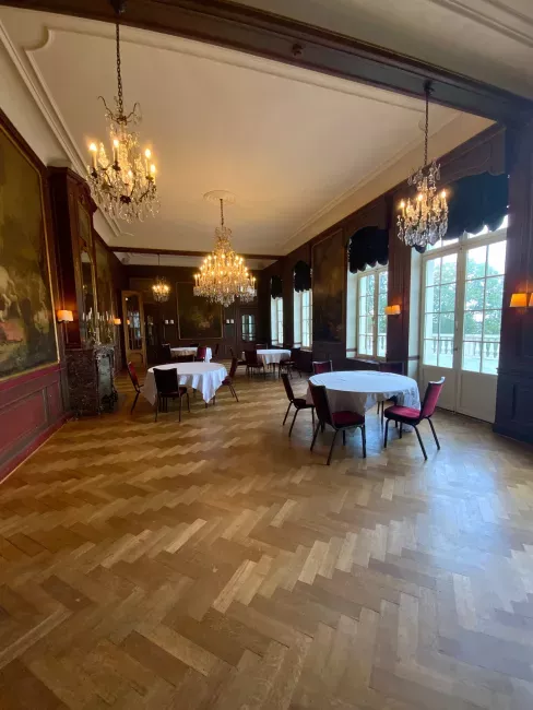 Grande salle élégante avec parquet en chevrons, lustres dorés et tables dispersées