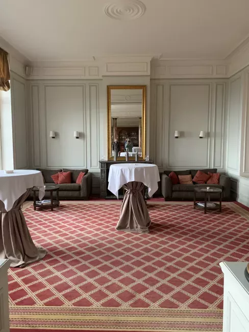 Salon spacieux avec deux canapés bordeaux, tapis à motifs géométriques et murs blancs lambrissés