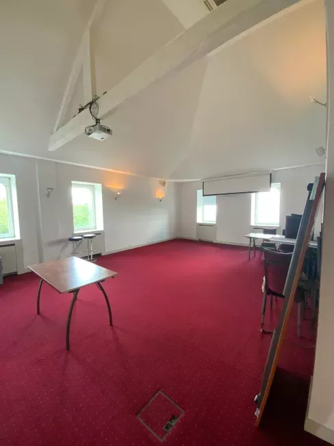 Salle intérieure avec moquette rouge, chaises pliantes et plafond voûté blanc