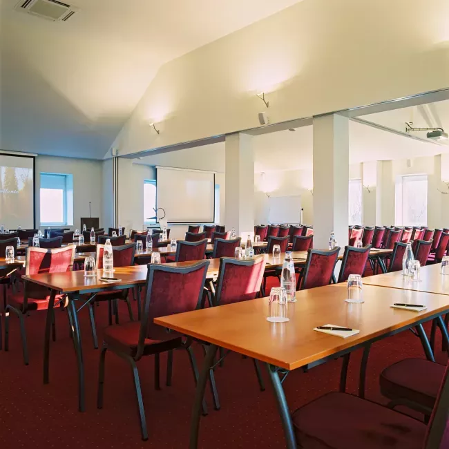 Salle de réunion avec tables en bois et chaises rouges disposées en rangées