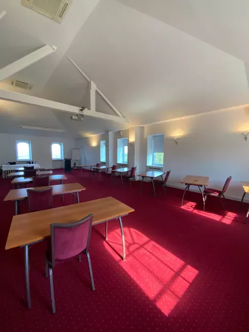 Intérieur d'une salle de réunion avec moquette rouge, tables en bois et plafond blanc lumineux